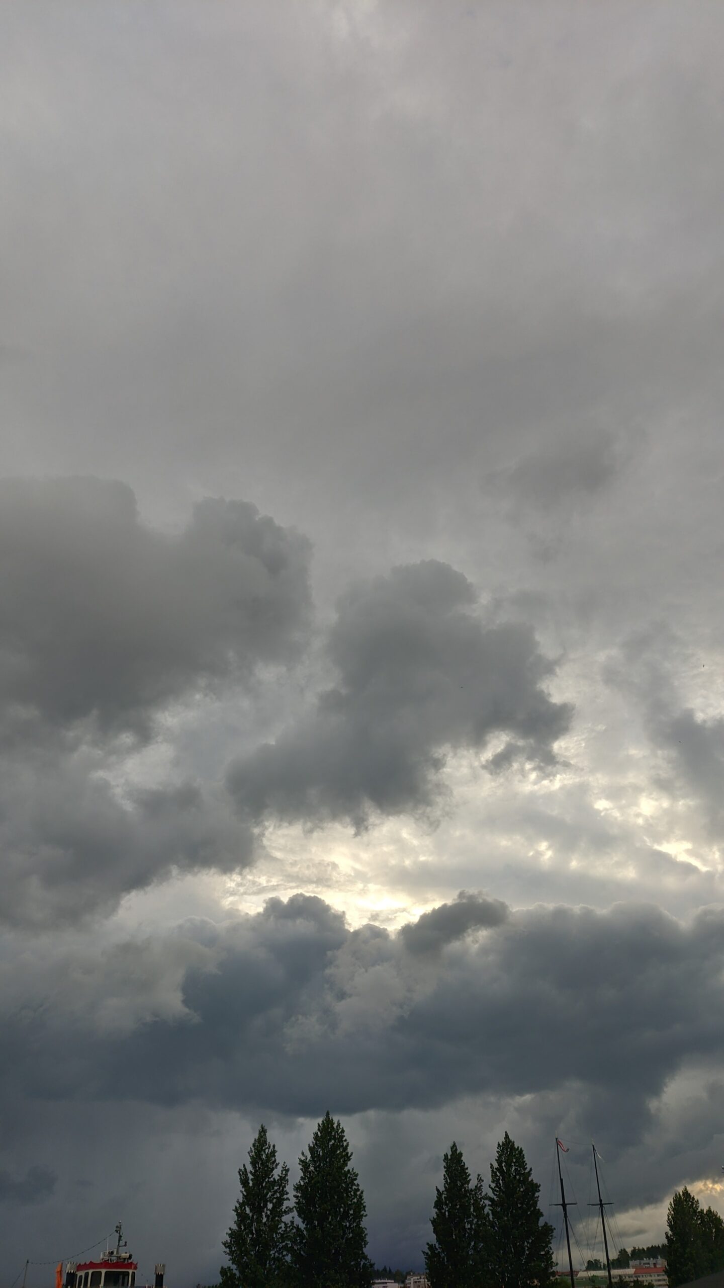 Kuva pilvistä sataman lähettyvillä. Taivaassa on reikä, josta tulee valoa, muuten tummaa pilveä.