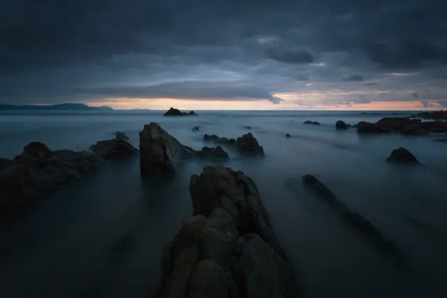 rock formations on body of water under cloudy sky