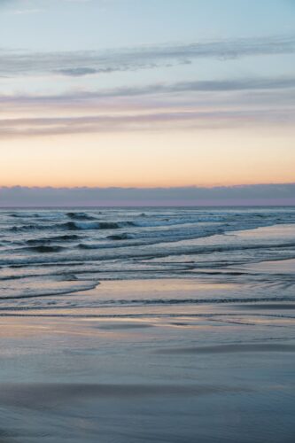 A person walking on the beach carrying a surfboard